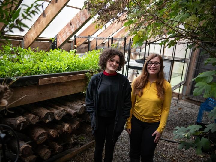 Two students stand in front of greenhouse at the radix center for public health coursework