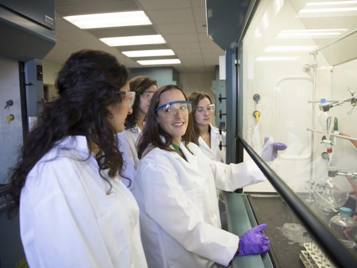 在化学通风柜工作的学生穿着实验室工作服、手套和安全眼镜